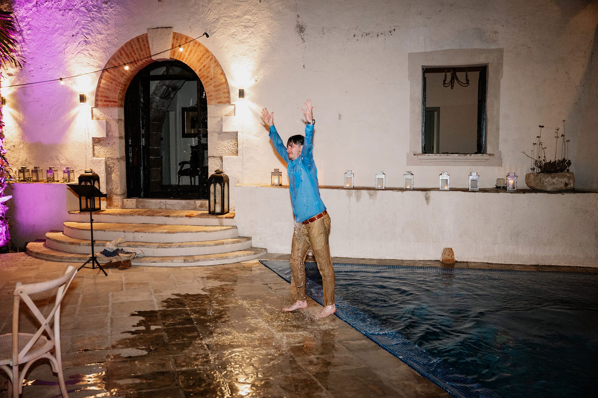 Man in wet clothes jumps into a pool at night with string lights - Barcelona Wedding Photographer