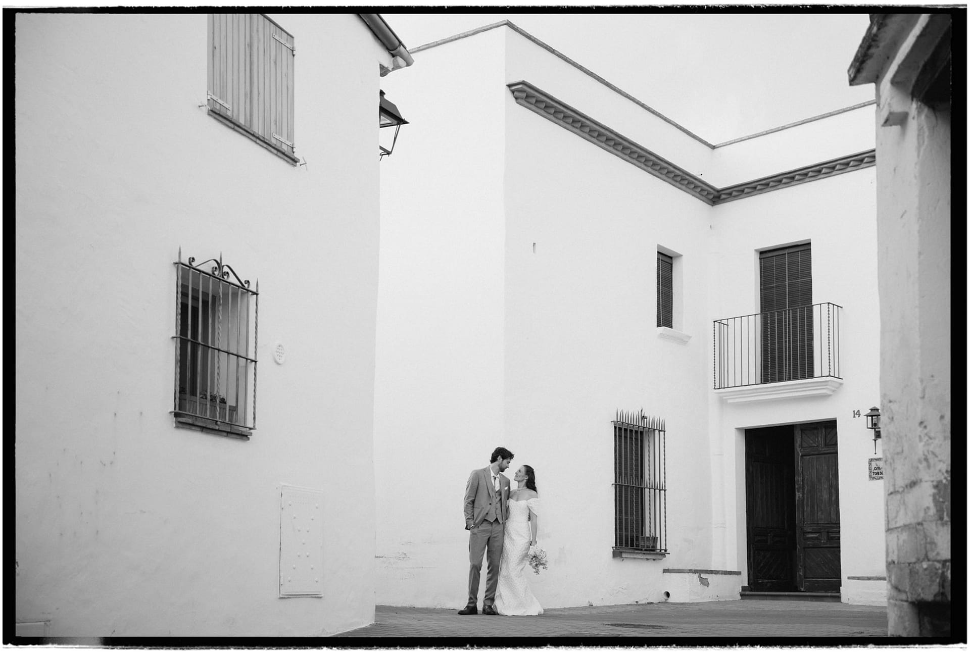 Bride and groom embrace in a white courtyard with traditional Spanish architecture. - Analog Wedding Photographer