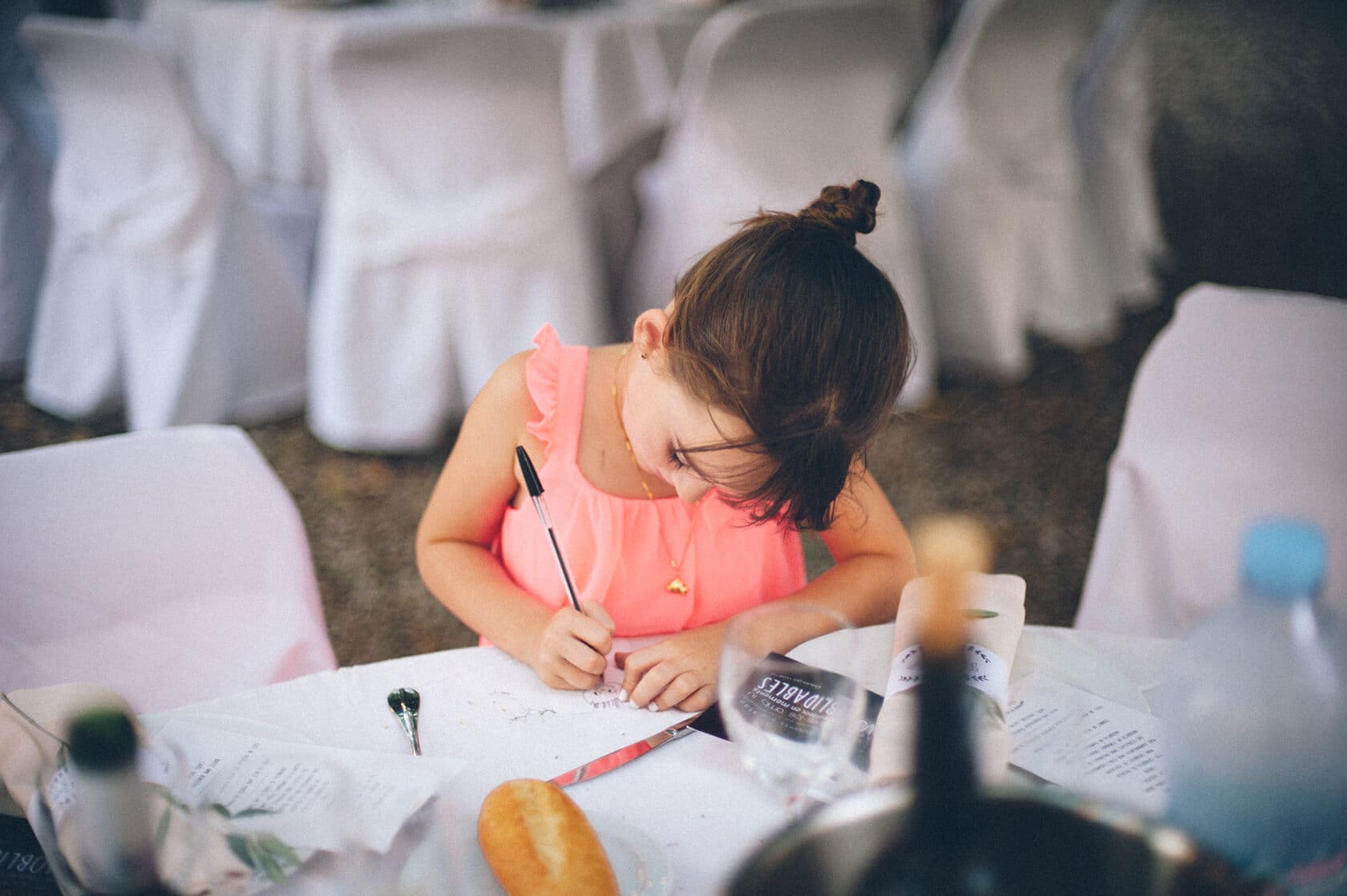 Young girl in a pink dress writes at a wedding reception table - Barcelona Wedding Photographer