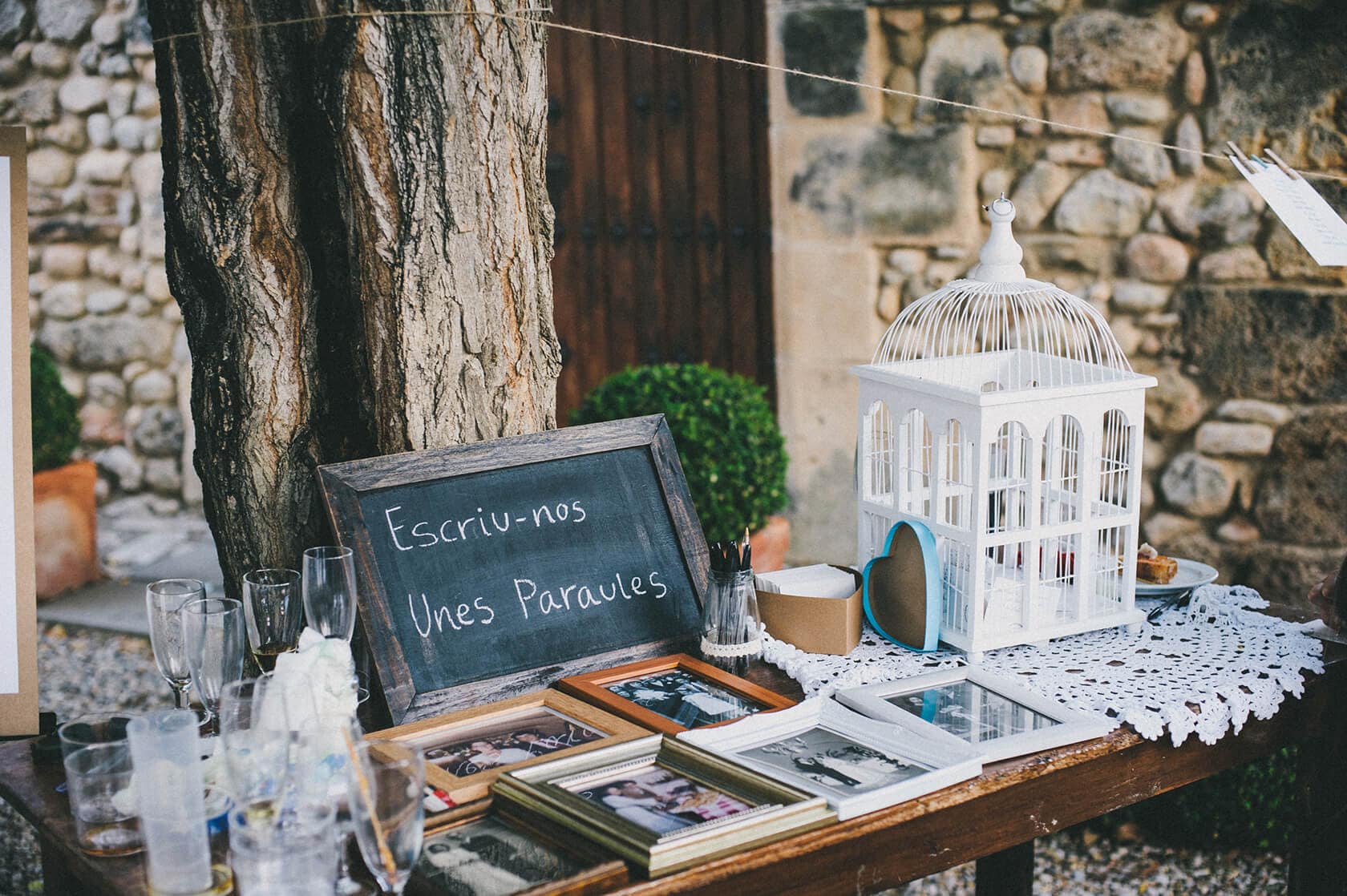 Wedding guest book with "Escriu-nos unes paraules" sign, photos, and birdcage - Barcelona Wedding Photographer