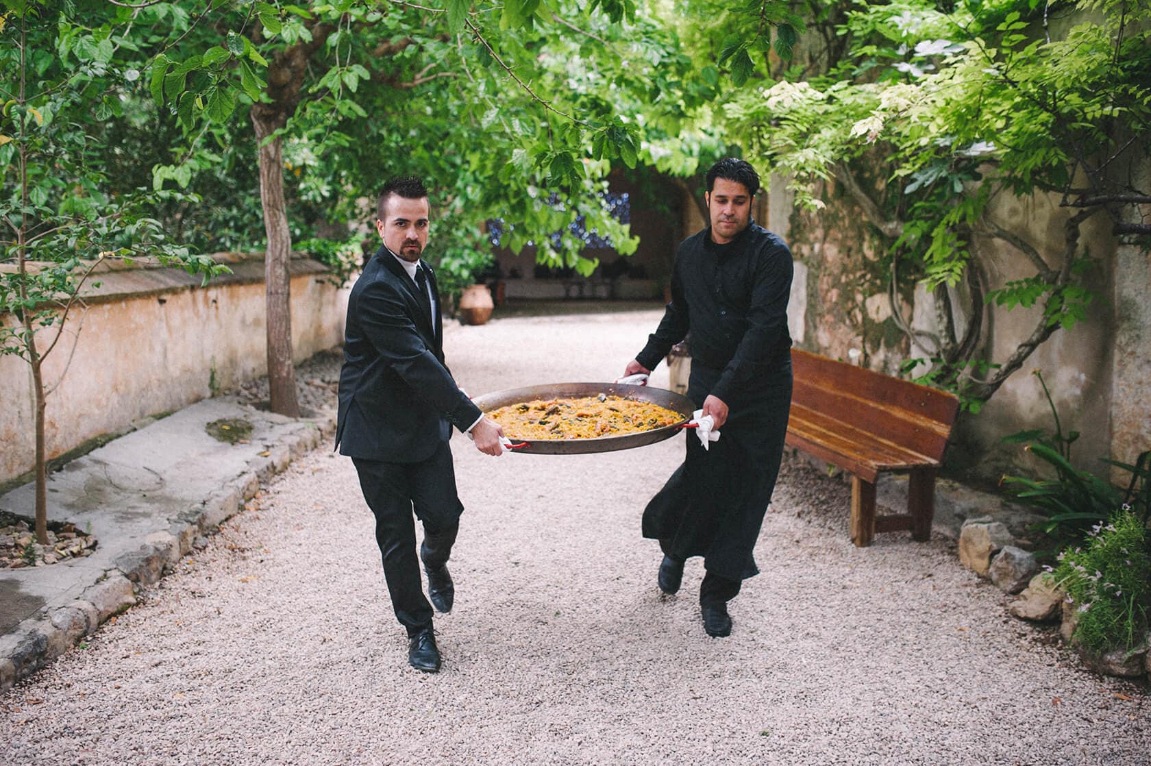 Waiters carry large paella dish at Villa Almanita wedding in Sitges - Barcelona Wedding Photographer
