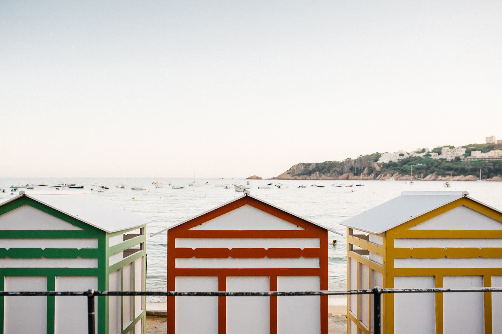 Colorful beach huts on S'Agaro, Spain, with the sea and hills in the background. - Barcelona Wedding Photographer