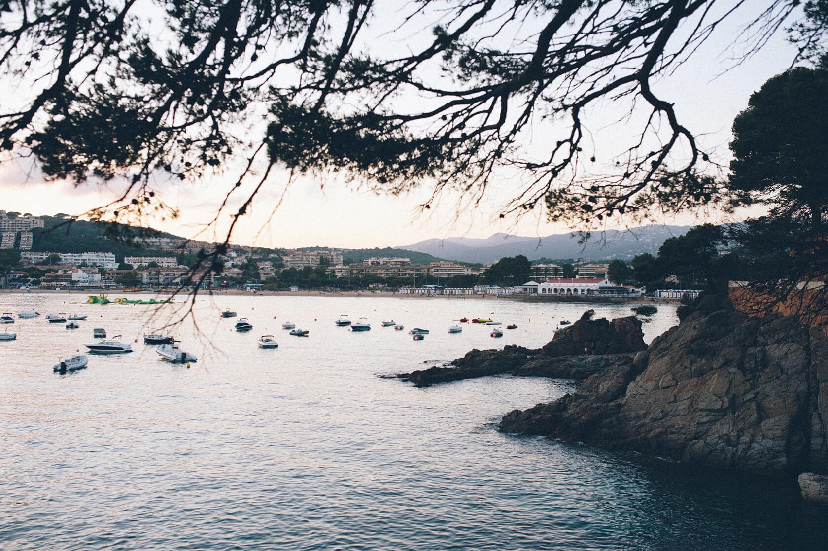 Boats anchored in a bay near S'Agaro, Spain, with a coastal town in the background. - Barcelona Wedding Photographer