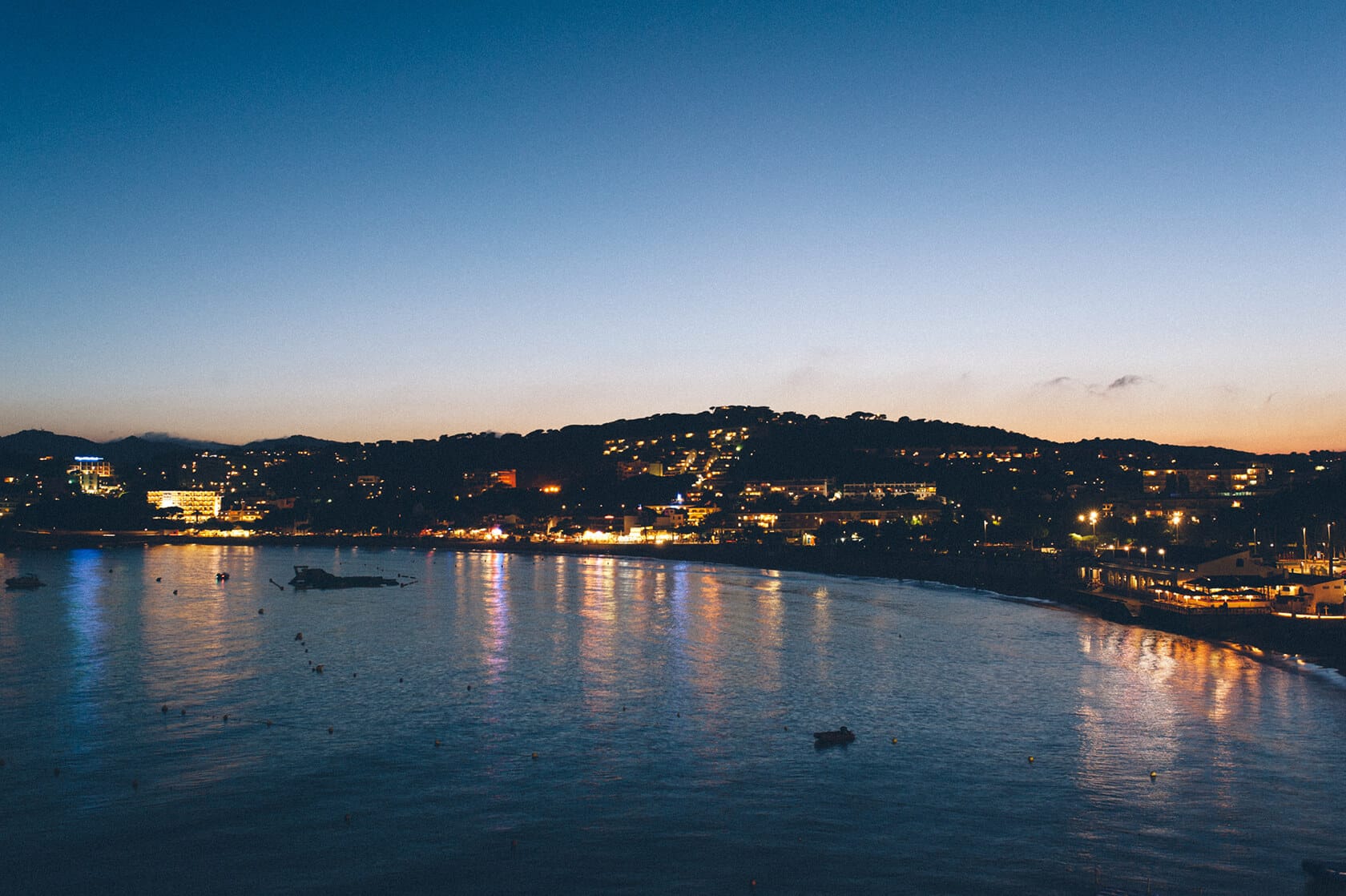 Coastal town lights reflect on the sea at dusk, S'Agaro, Spain. - Barcelona Wedding Photographer