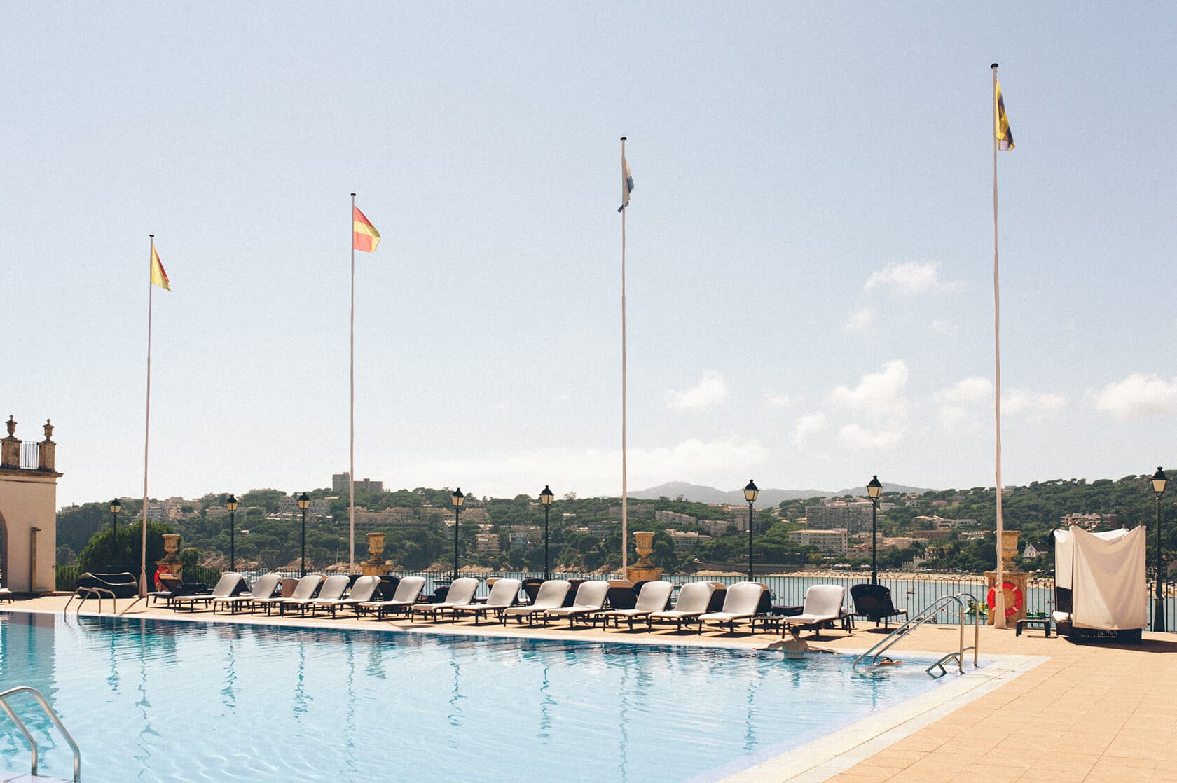 Tsega & Anders wedding photographer S'Agaro Spain: Poolside lounge chairs and flags at a sunny resort. - Barcelona Wedding Photographer