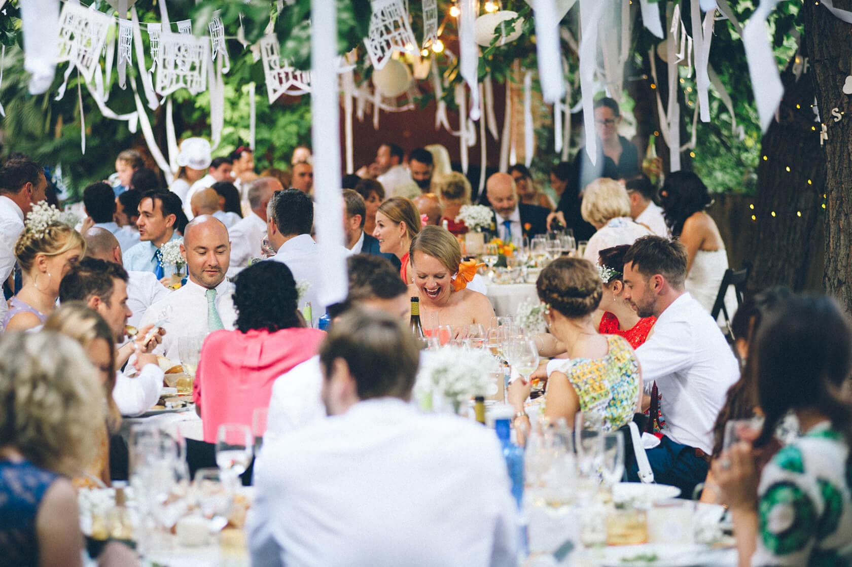 Wedding guests dining outdoors under festive decorations at a villa in Sitges. - Barcelona Wedding Photographer