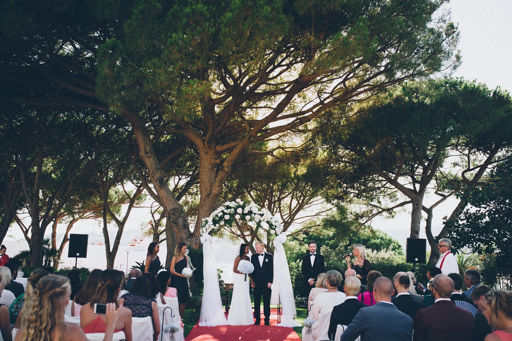 Tsega & Anders wedding ceremony in S'Agaro, Spain, with guests under a tree. - Barcelona Wedding Photographer