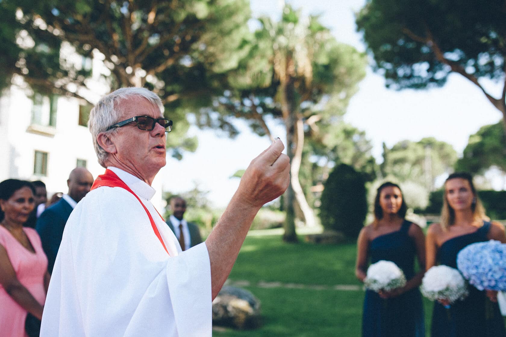 Wedding officiant leads ceremony in S'Agaro, Spain, with bridesmaids nearby. - Barcelona Wedding Photographer
