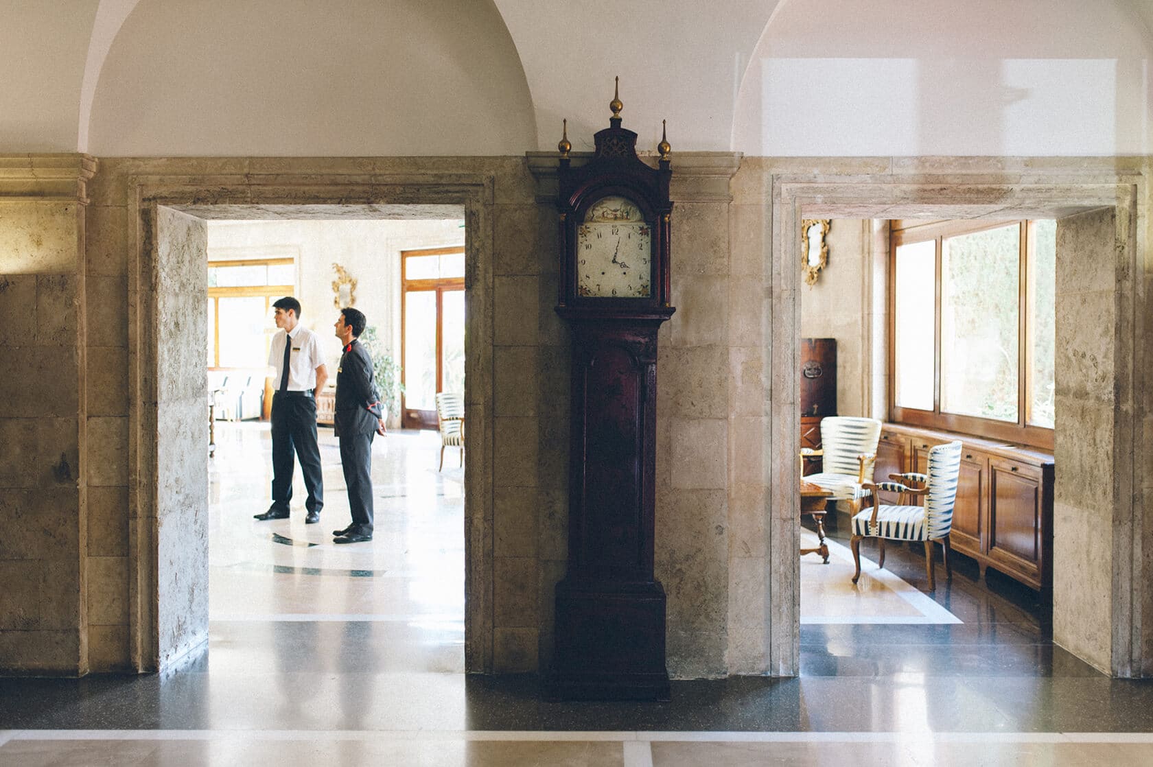 Tsega & Anders wedding photographer S'Agaro: Two men in suits in a grand hall with a grandfather clock. - Barcelona Wedding Photographer