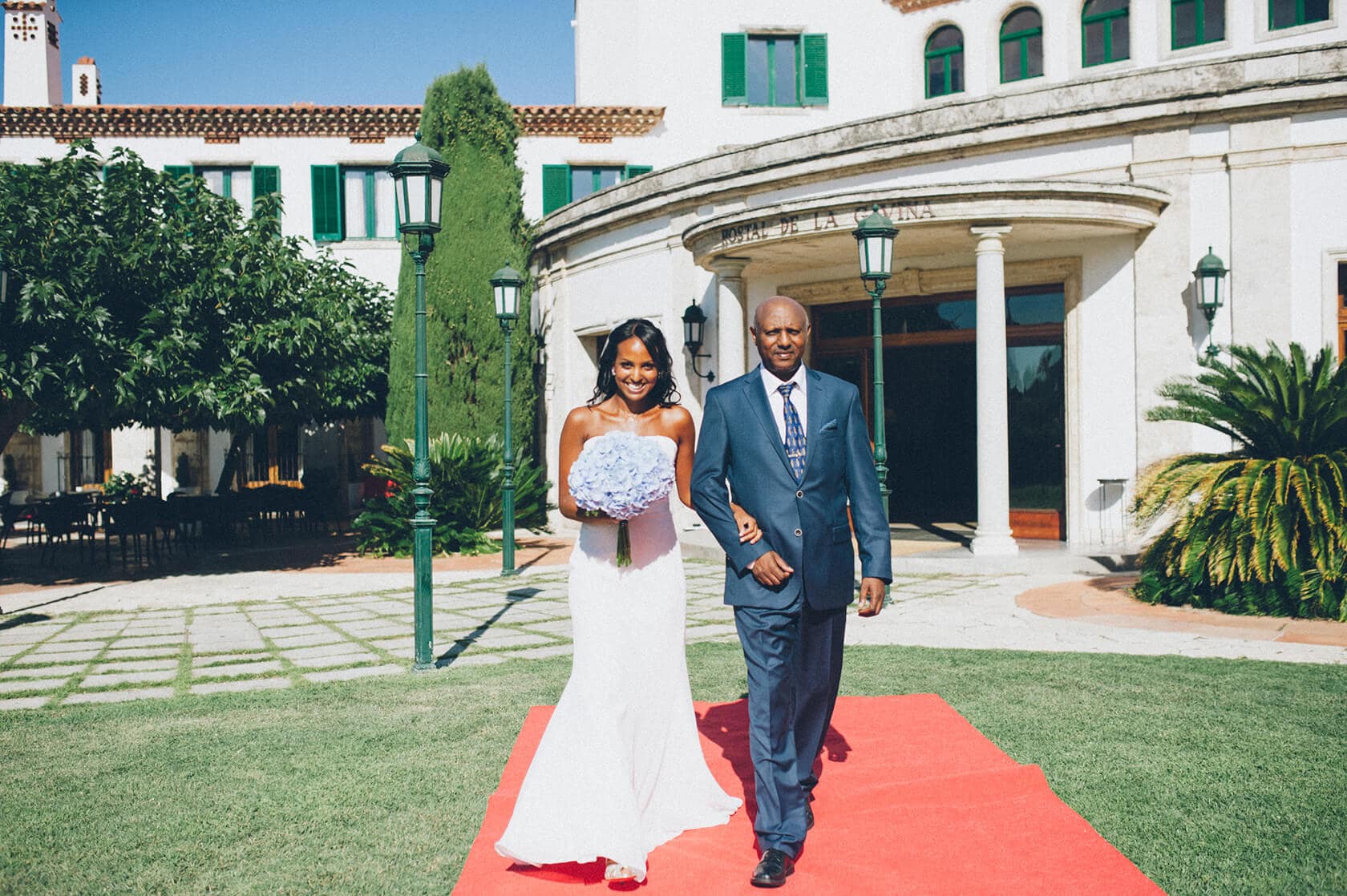 Bride and father walk down red carpet at wedding in S'Agaro, Spain. - Barcelona Wedding Photographer