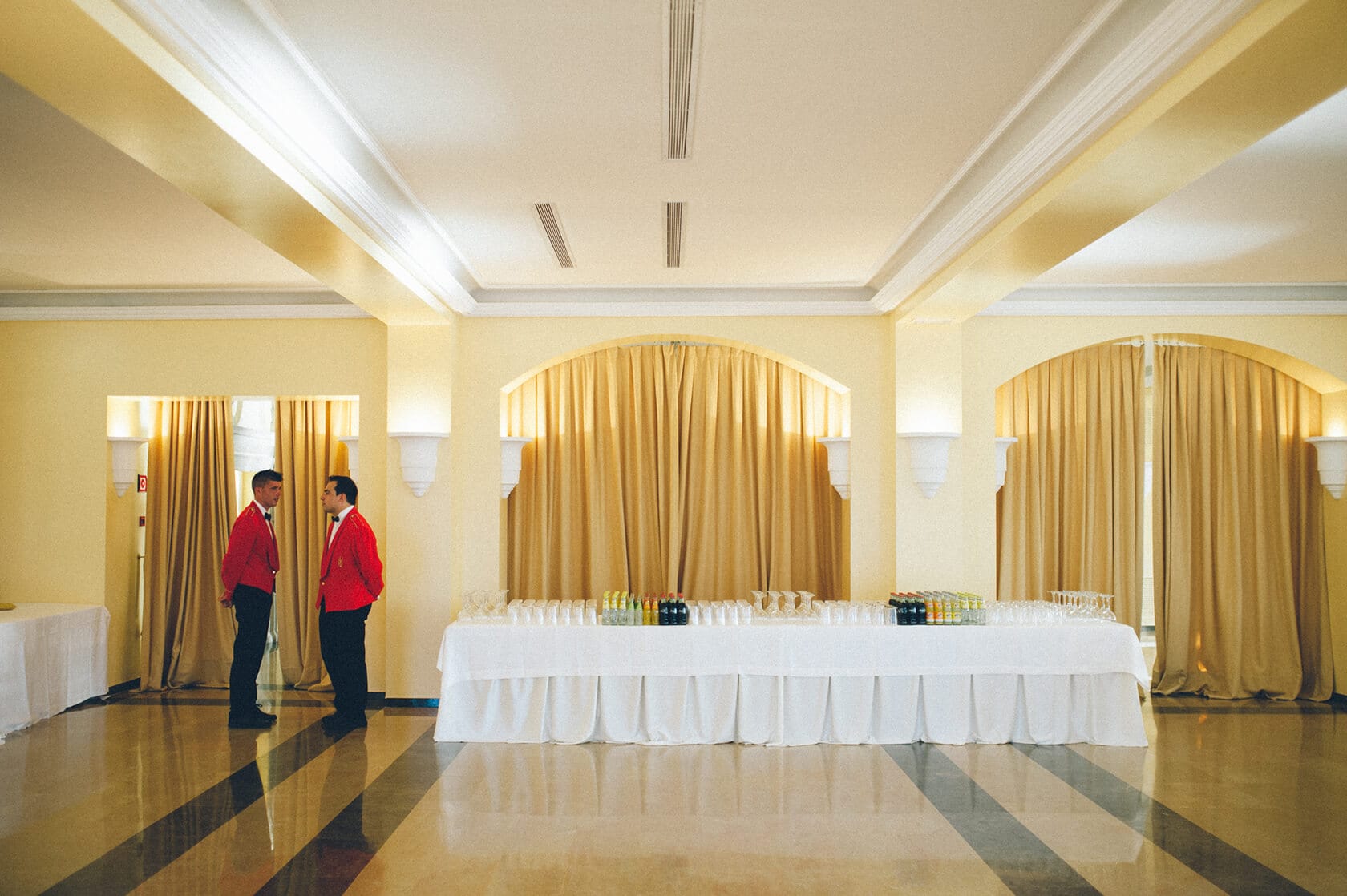Catering staff in red jackets stand by a banquet table at a wedding in S'Agaro, Spain. - Barcelona Wedding Photographer