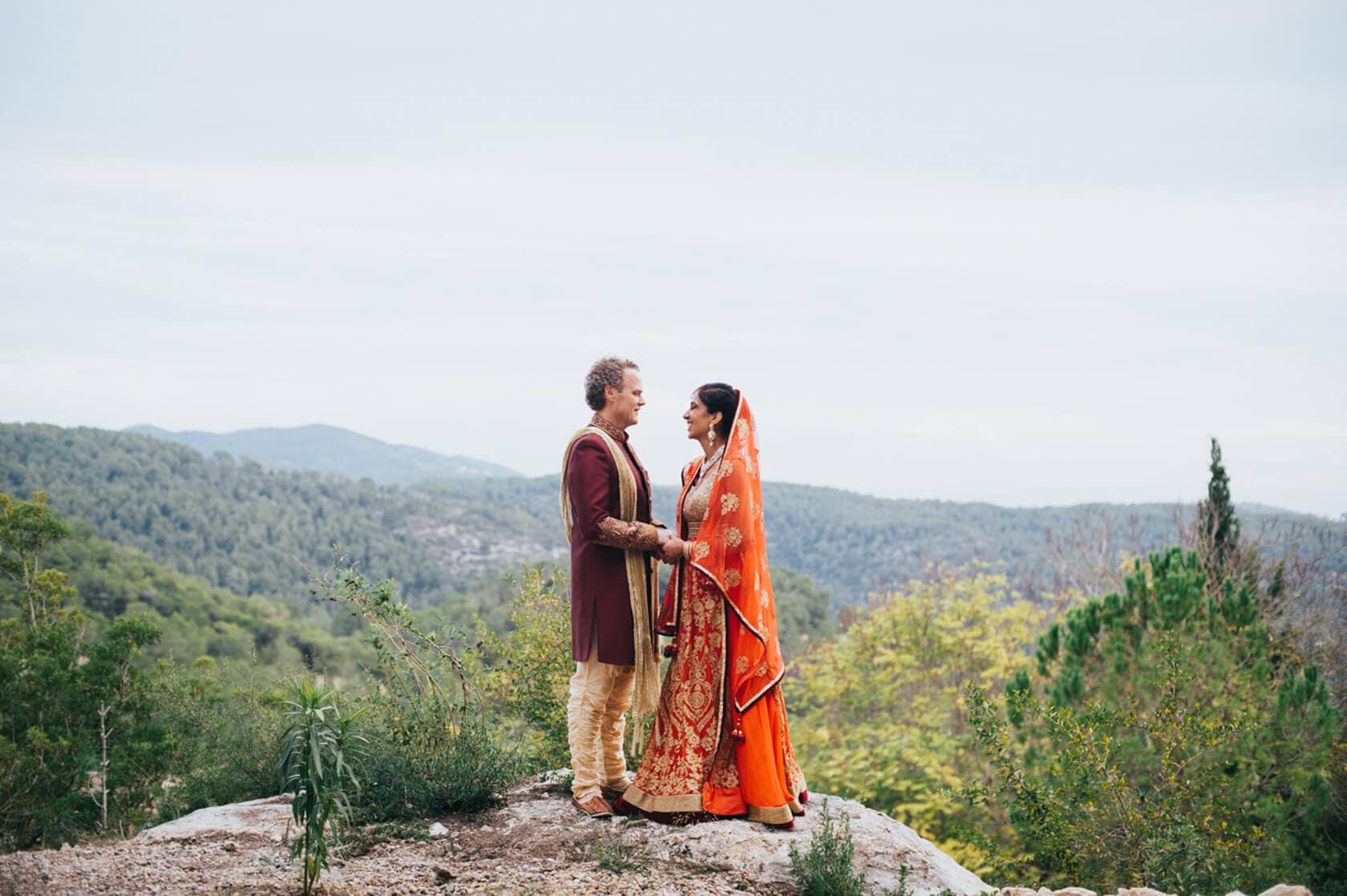 Couple in Indian wedding attire on a hilltop overlooking Sitges landscape - Barcelona Wedding Photographer