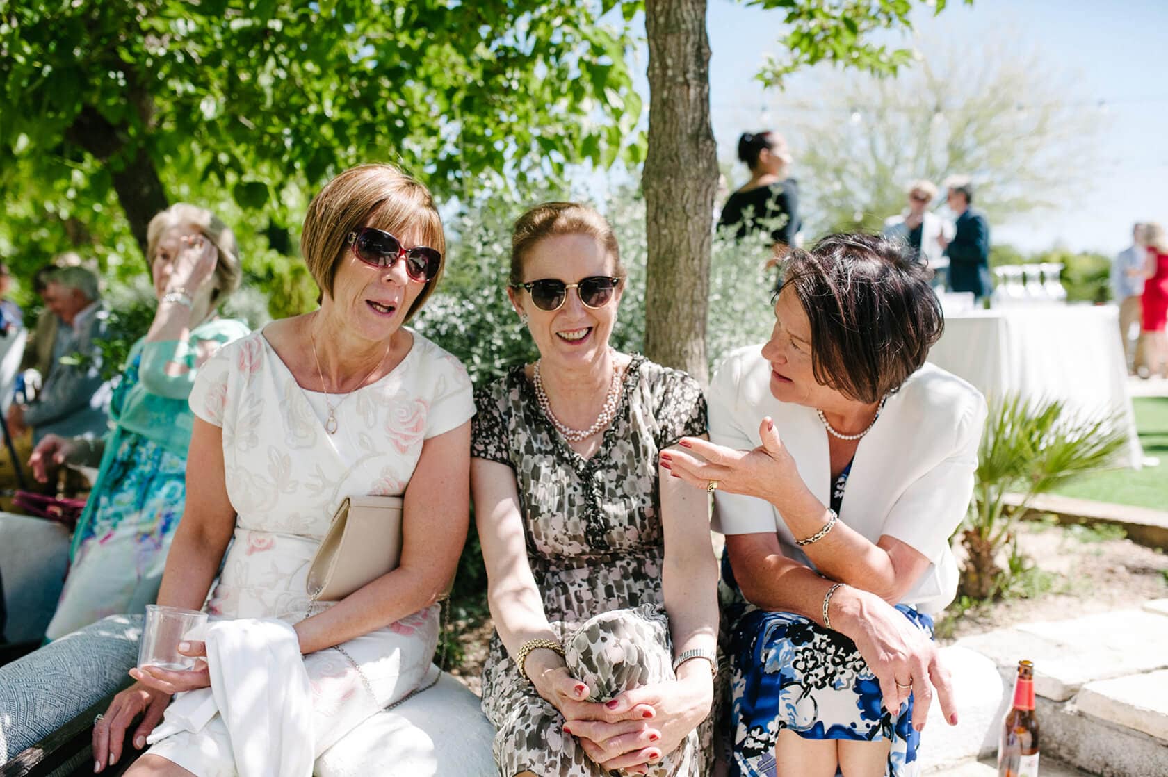 Three women in summer dresses chat at a Casanova Estate wedding. - Barcelona Wedding Photographer
