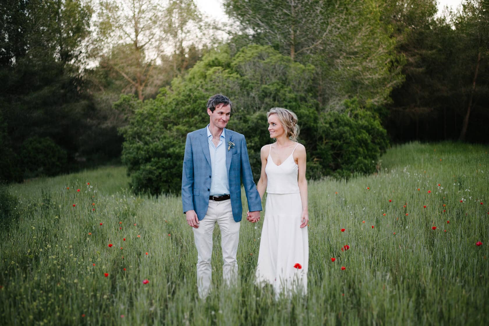 Catherine and James holding hands in a field of poppies at Casanova Estate wedding venue. - Barcelona Wedding Photographer