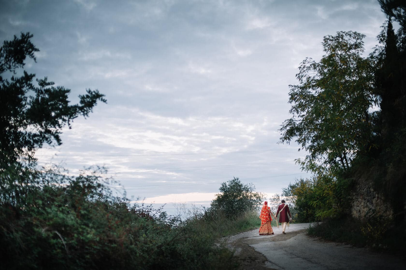 Couple in traditional Indian wedding attire walking on a path near a wedding villa in Sitges - Barcelona Wedding Photographer