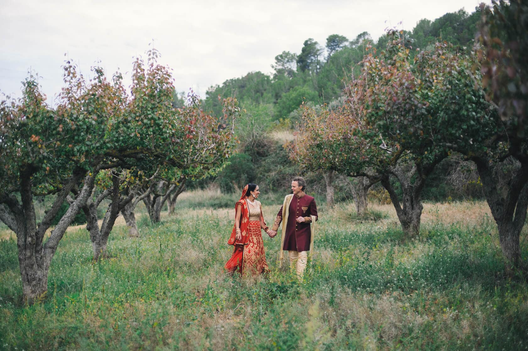 Couple in traditional Indian wedding attire walking in a garden, wedding villas Sitges - Barcelona Wedding Photographer