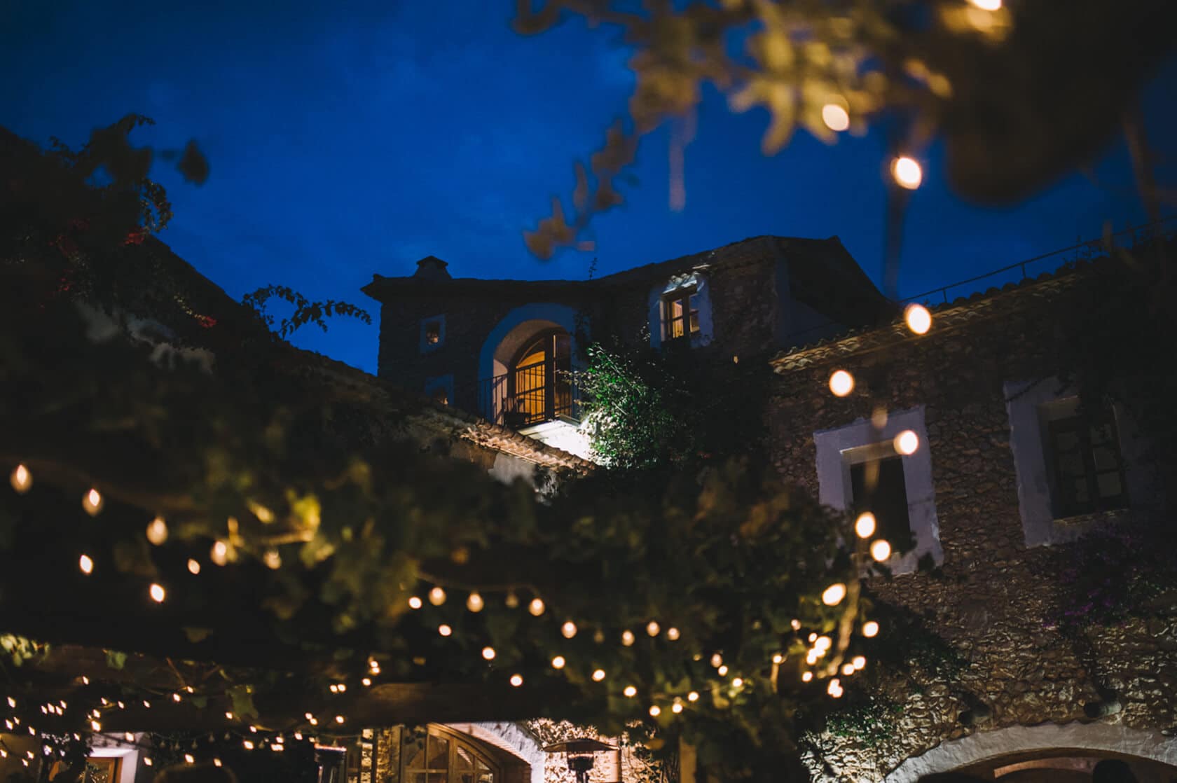 Twinkling string lights illuminate a stone villa at dusk, ideal for weddings in Sitges. - Barcelona Wedding Photographer