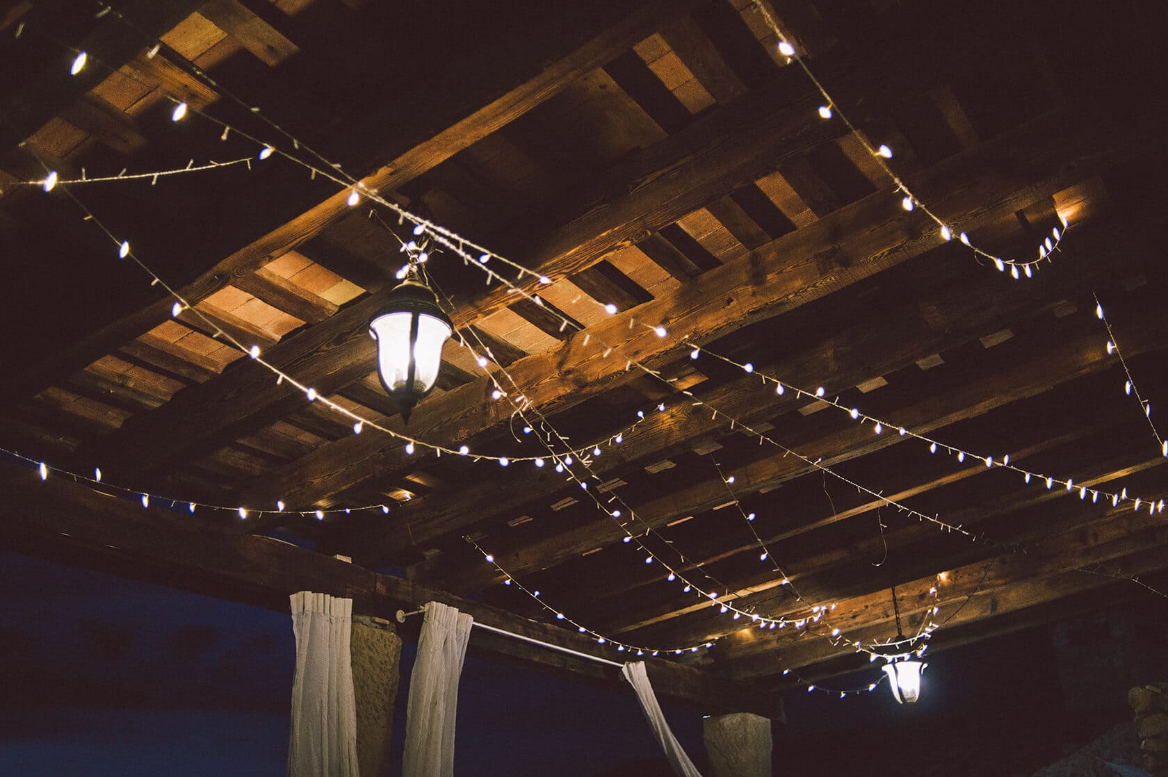 String lights and lanterns illuminate a wooden pergola at a wedding villa in Sitges. - Barcelona Wedding Photographer
