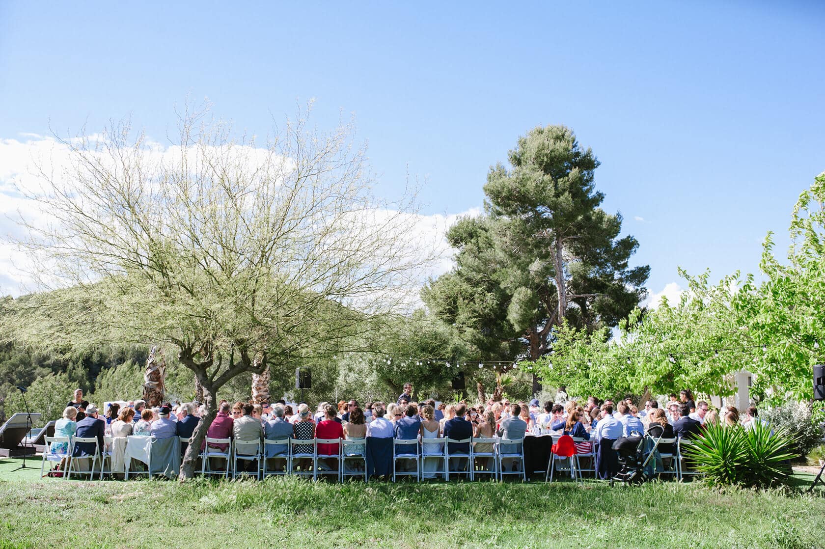Outdoor wedding reception in Sitges with guests seated at tables under trees. - Barcelona Wedding Photographer