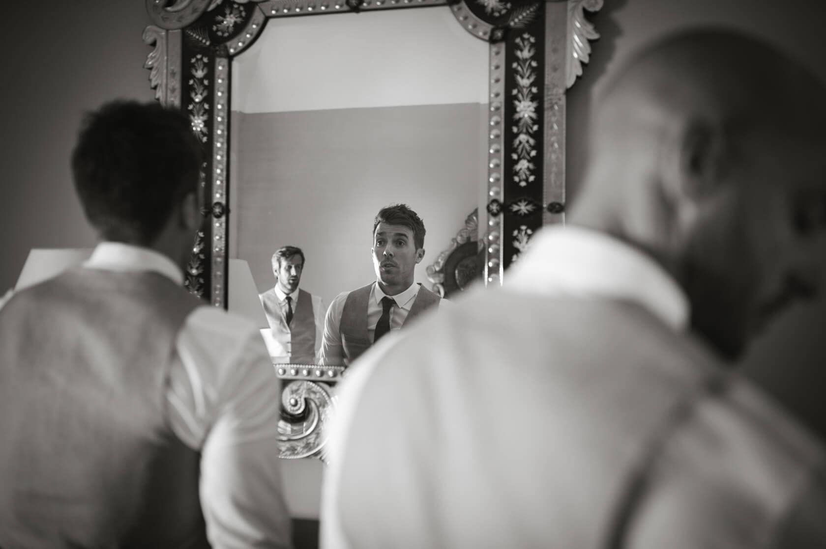 Groom adjusting tie in mirror before Sitges wedding. - Barcelona Wedding Photographer