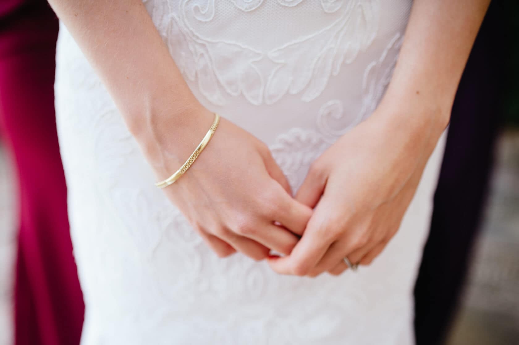 Bride's hands clasped, wearing a gold bracelet, with lace wedding dress detail. Fotografia Sitges Castell de Tamarit wedding. - Barcelona Wedding Photographer