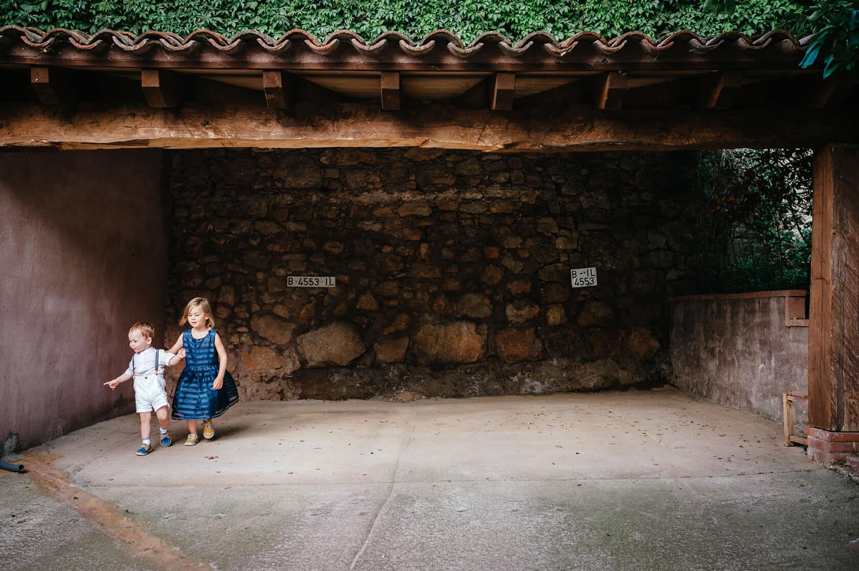 Two children in vintage clothing walk under a tiled overhang at a wedding venue. - Barcelona Wedding Photographer