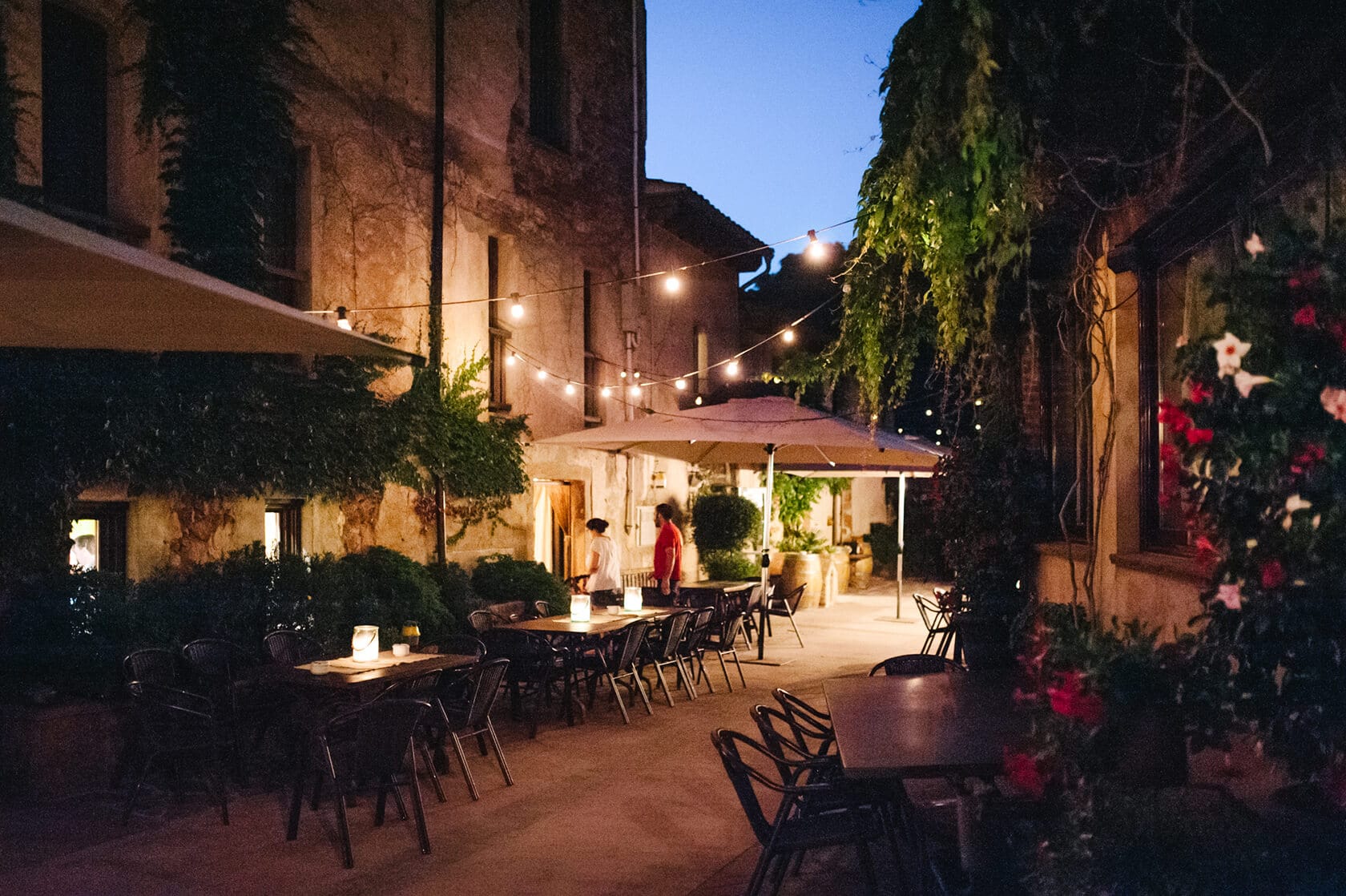 Romantic vintage style wedding reception at dusk with string lights and ivy-covered walls. - Barcelona Wedding Photographer