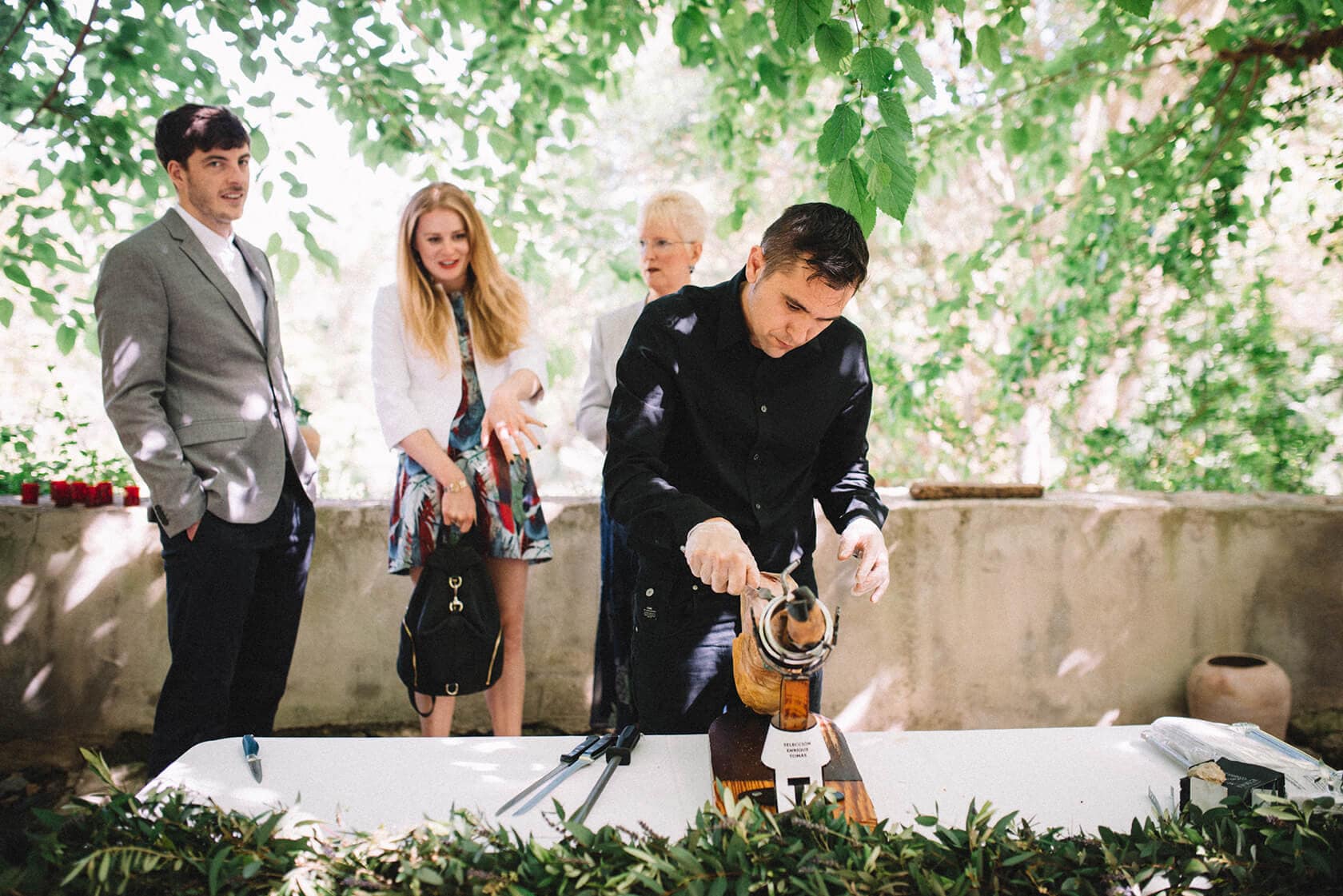 Clara & Toph destination wedding at Villa Almanita, Sitges: groom carves ham. - Barcelona Wedding Photographer