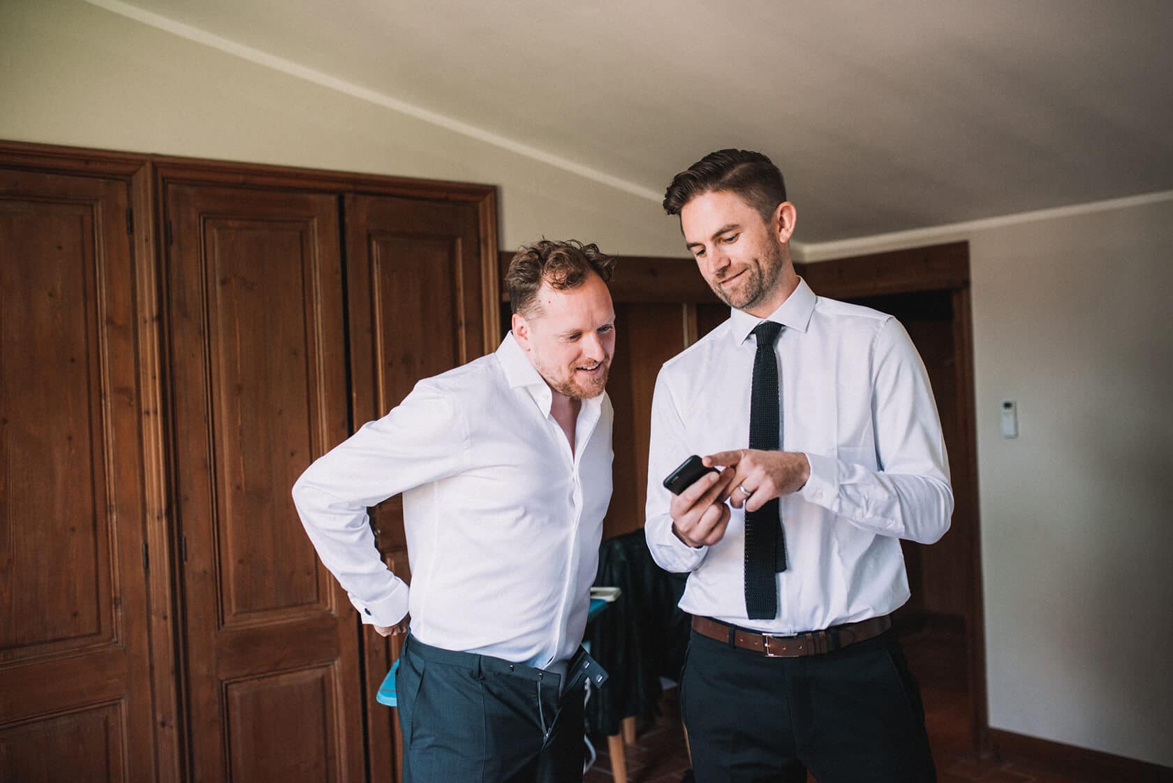 Groom and groomsman checking phone at Villa Almanita before destination wedding in Sitges. - Barcelona Wedding Photographer