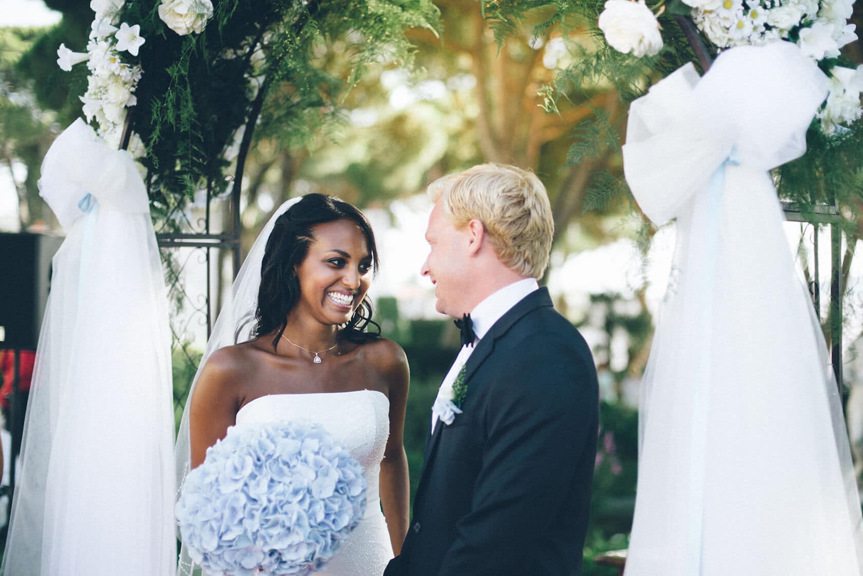 Bride and groom smiling at each other under wedding arch in S'Agaro - Barcelona Wedding Photographer