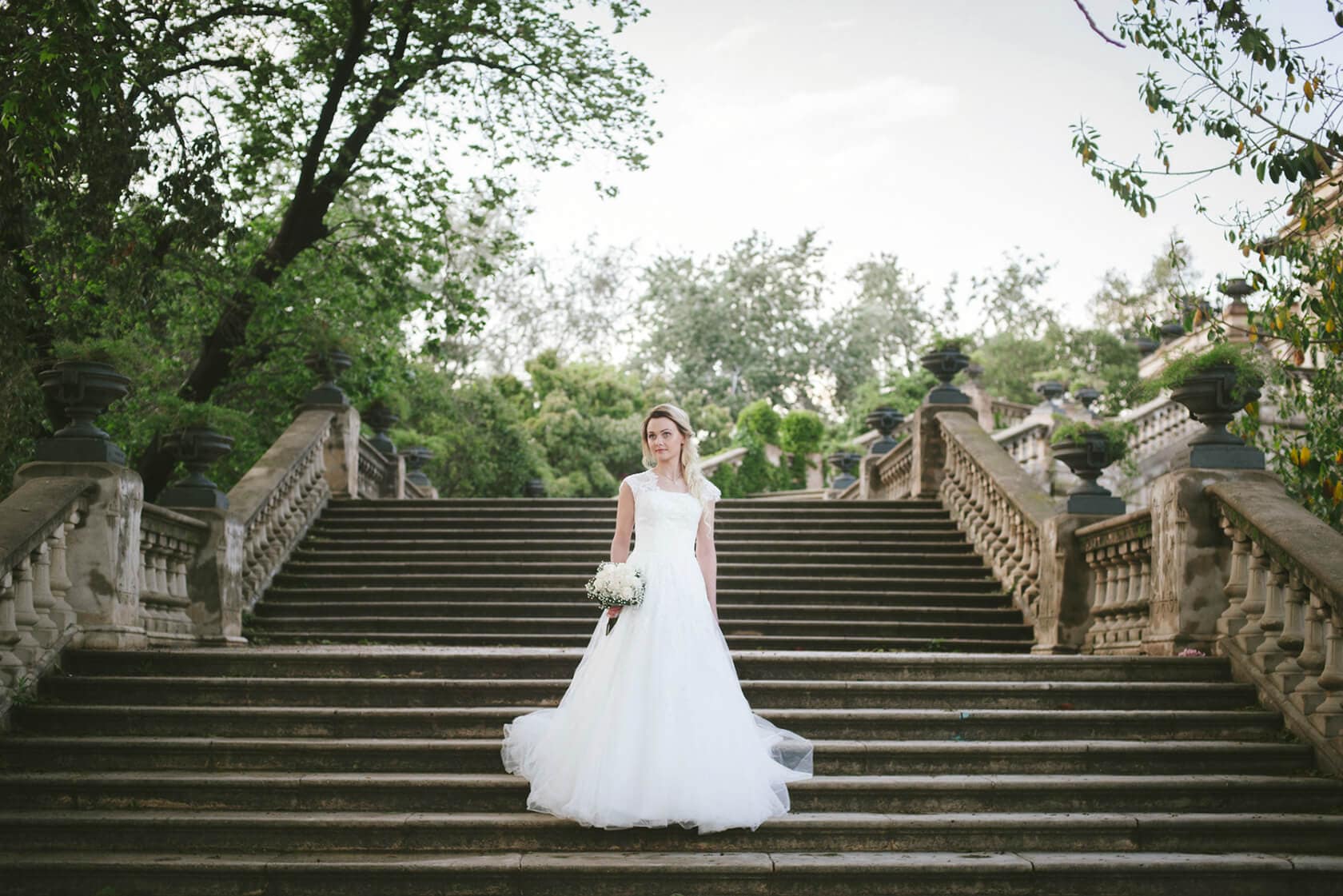 Bride in a white dress holding a bouquet on grand outdoor stairs in Barcelona - Barcelona Wedding Photographer