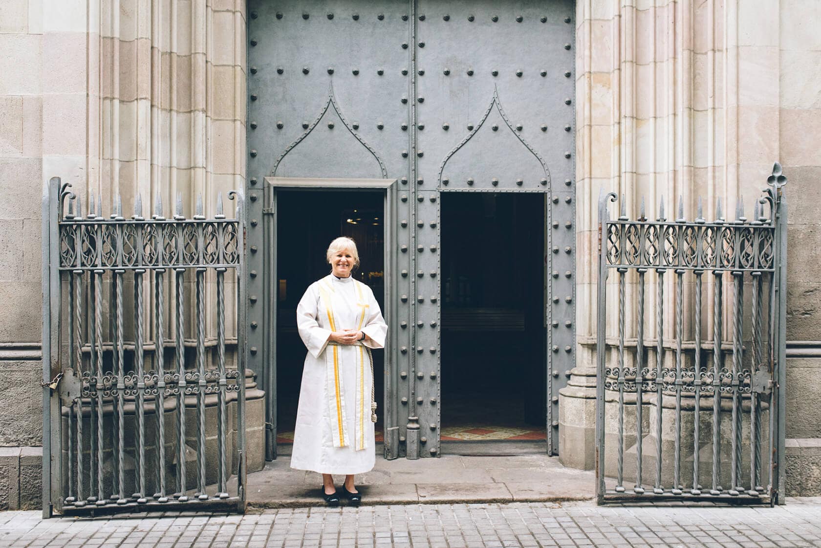 Woman in clergy attire stands before large church doors in Barcelona - Barcelona Wedding Photographer