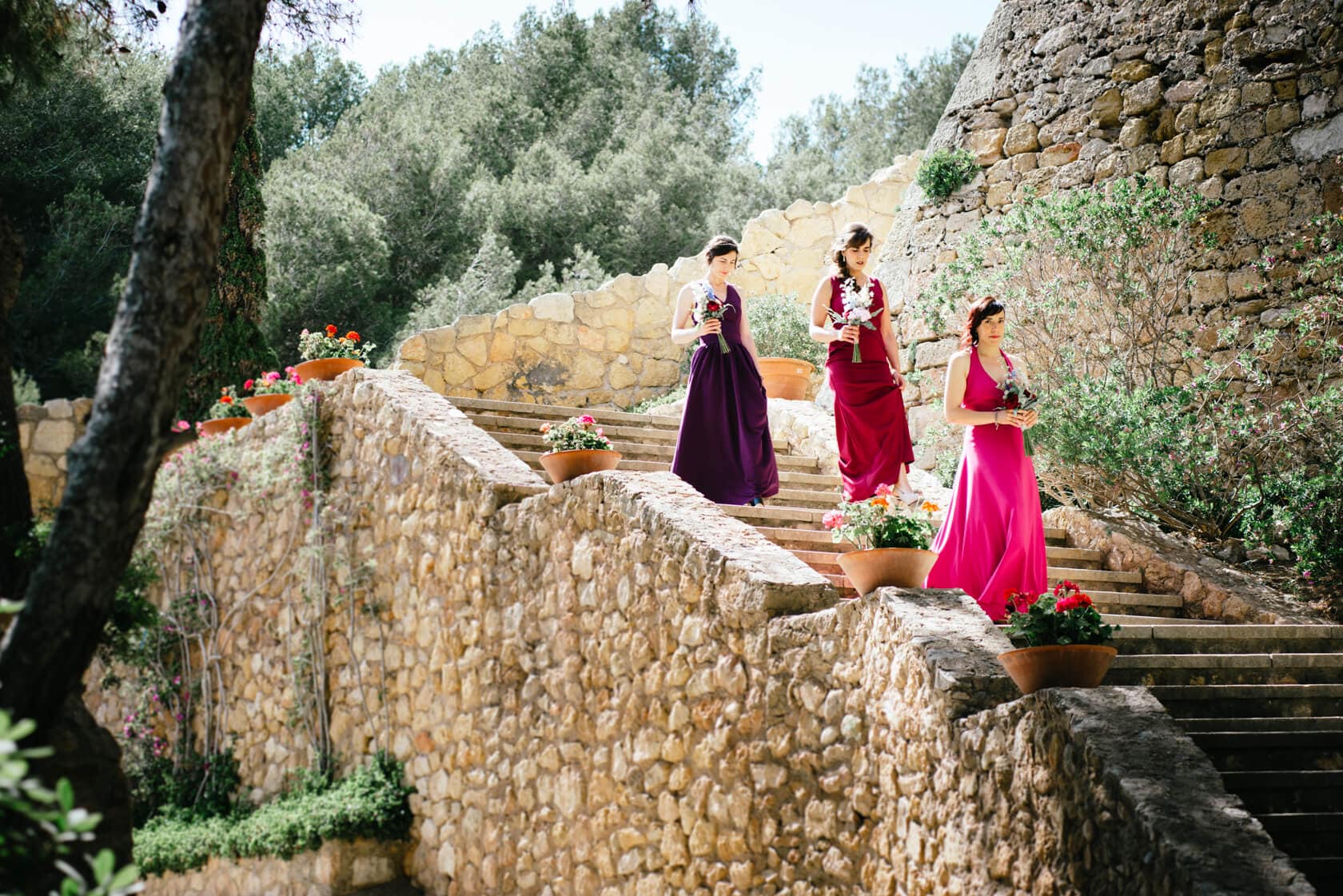 Bridesmaids in colorful gowns descend stone steps at Castell de Tamarit wedding. - Barcelona Wedding Photographer