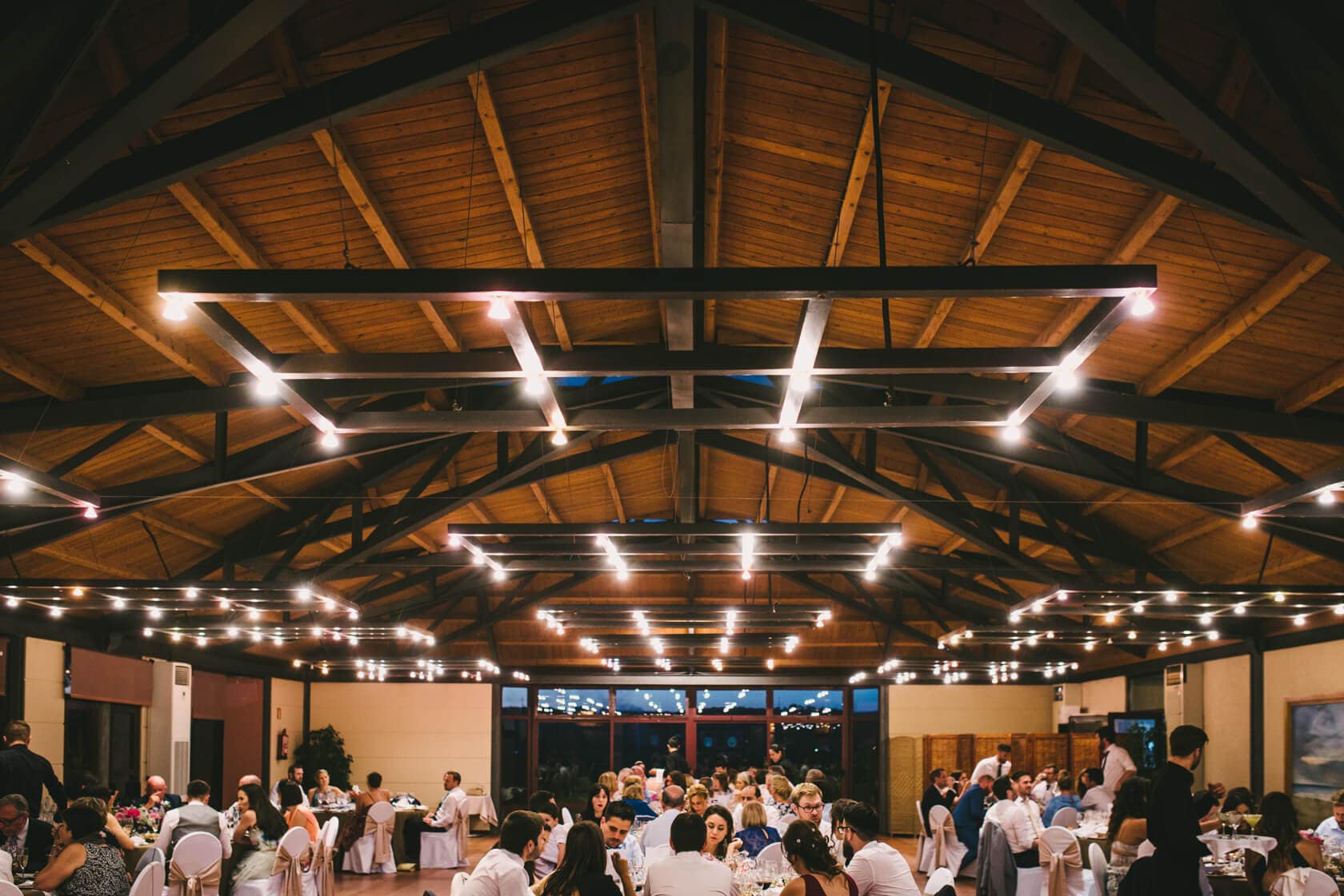 Wedding reception at Castell de Tamarit, Sitges, with guests seated at tables under a rustic wooden ceiling. - Barcelona Wedding Photographer
