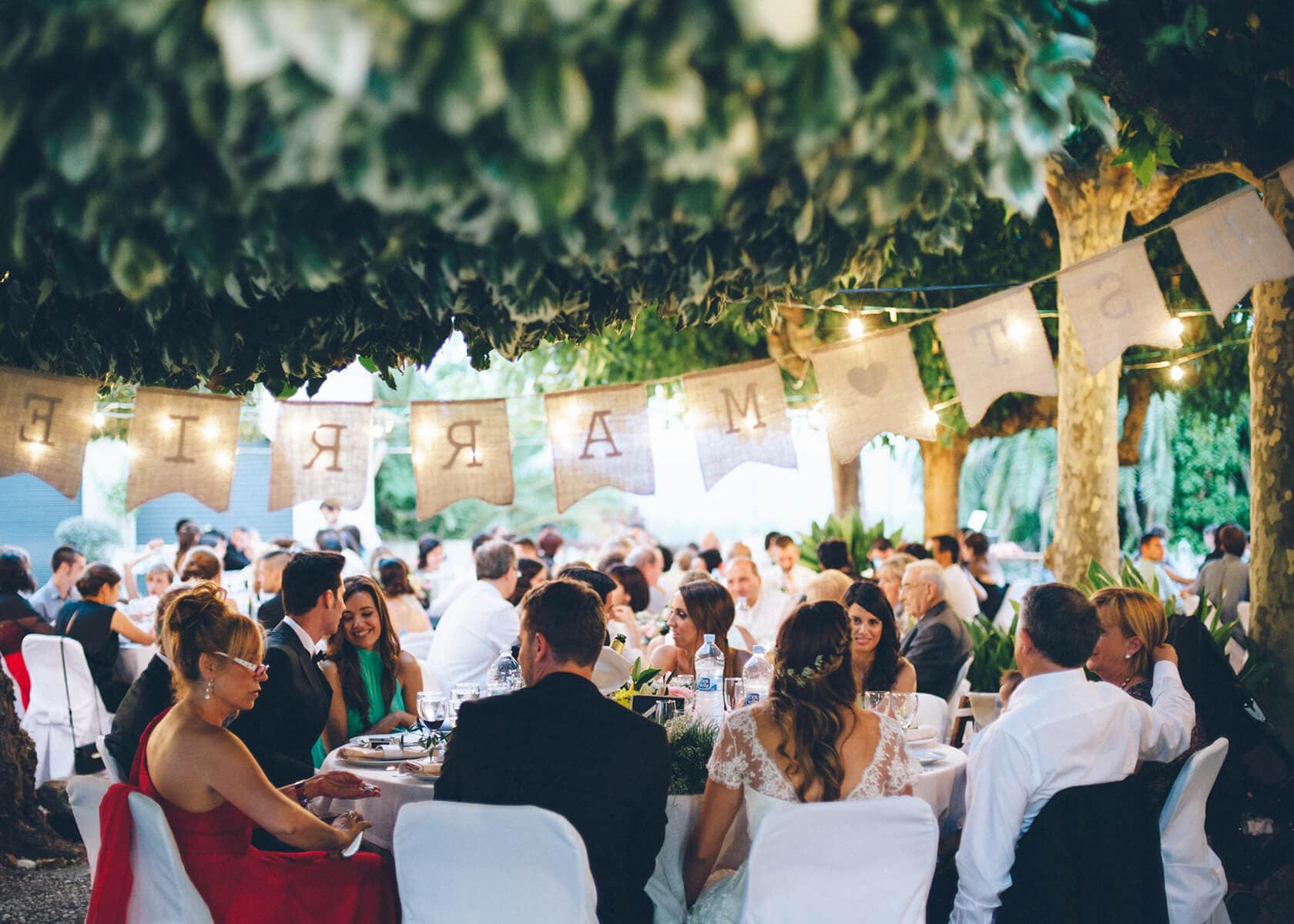 Cris & Rafa's wedding reception: guests dining outdoors under trees with string lights. - Barcelona Wedding Photographer