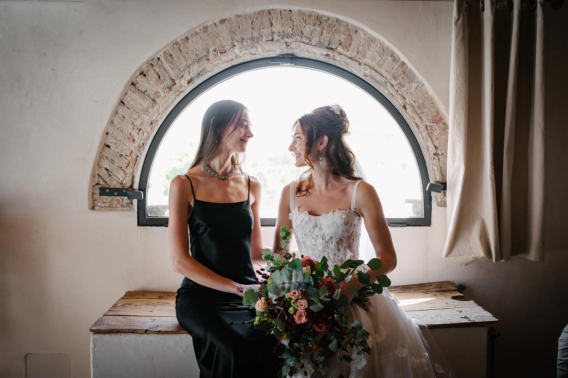 Bride and bridesmaid in black dress with bouquet, Masia Victoria wedding. - Sitges Wedding Photographer