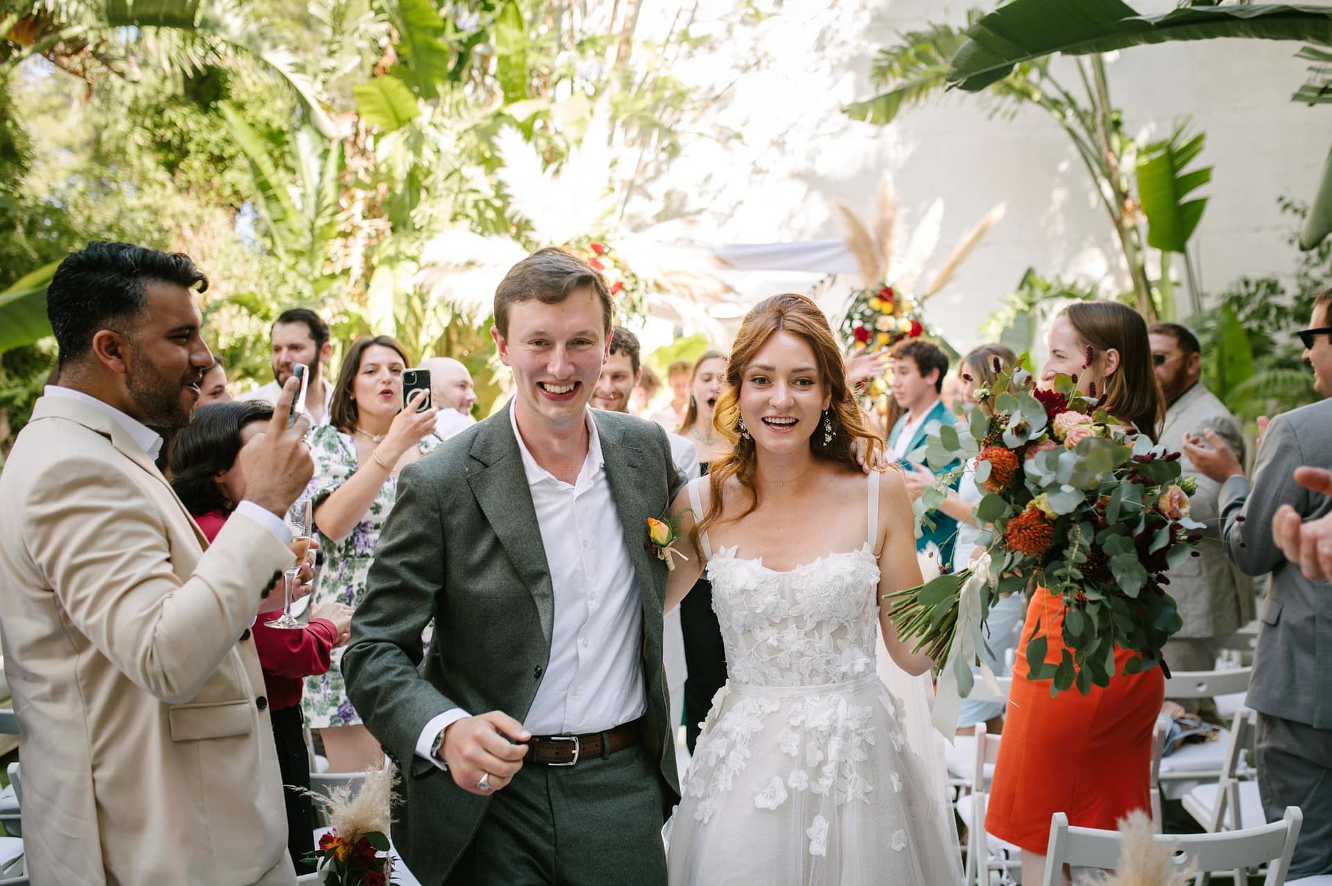 Masia Victoria a joyful wedding couple, walk down the aisle surrounded by guests. - Sitges Wedding Photographer
