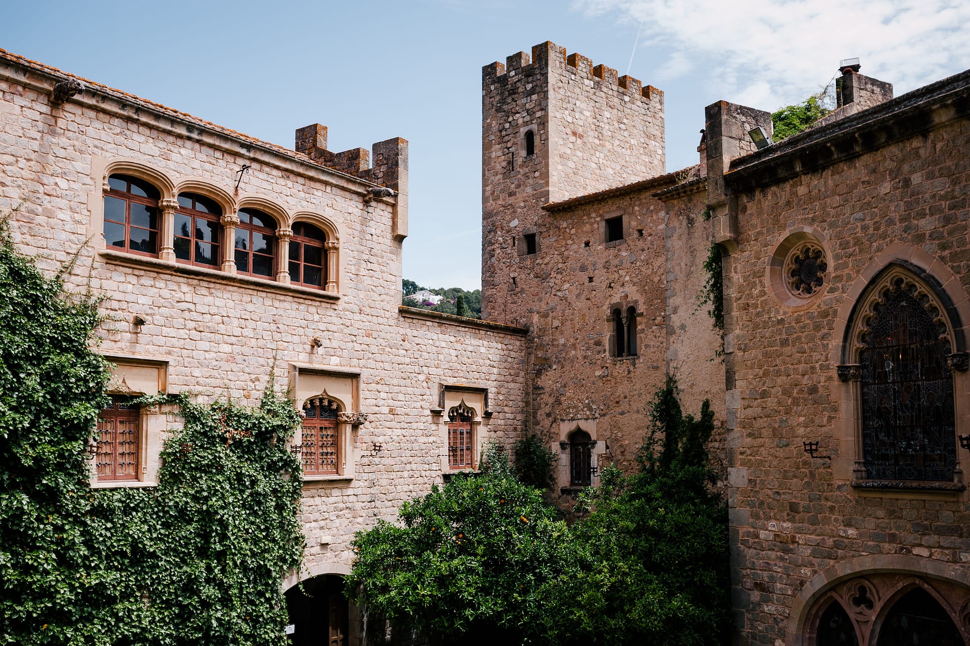 Stone courtyard of a medieval castle with ivy-covered walls and arched windows. - Barcelona Wedding Venues